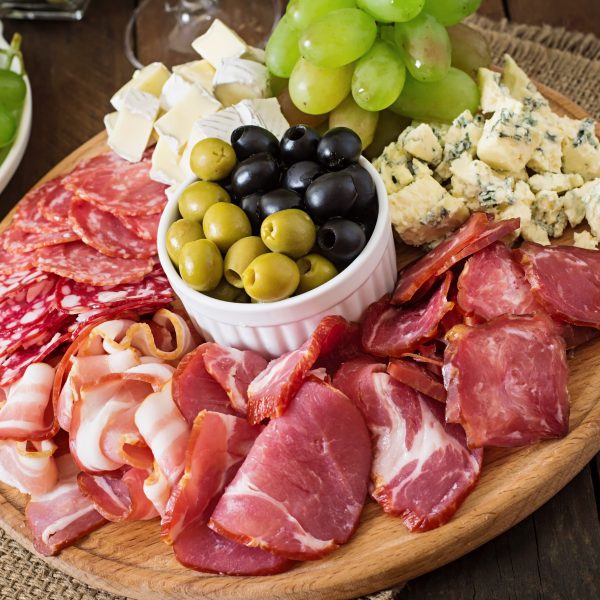 Antipasto catering platter with bacon, jerky, salami, cheese and grapes on a wooden background